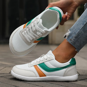 White sneakers with green and orange accents worn by a person on a wooden floor.