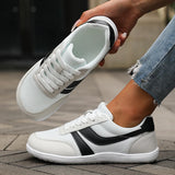 White sneakers with black accents held by a person wearing jeans on a wooden floor.
