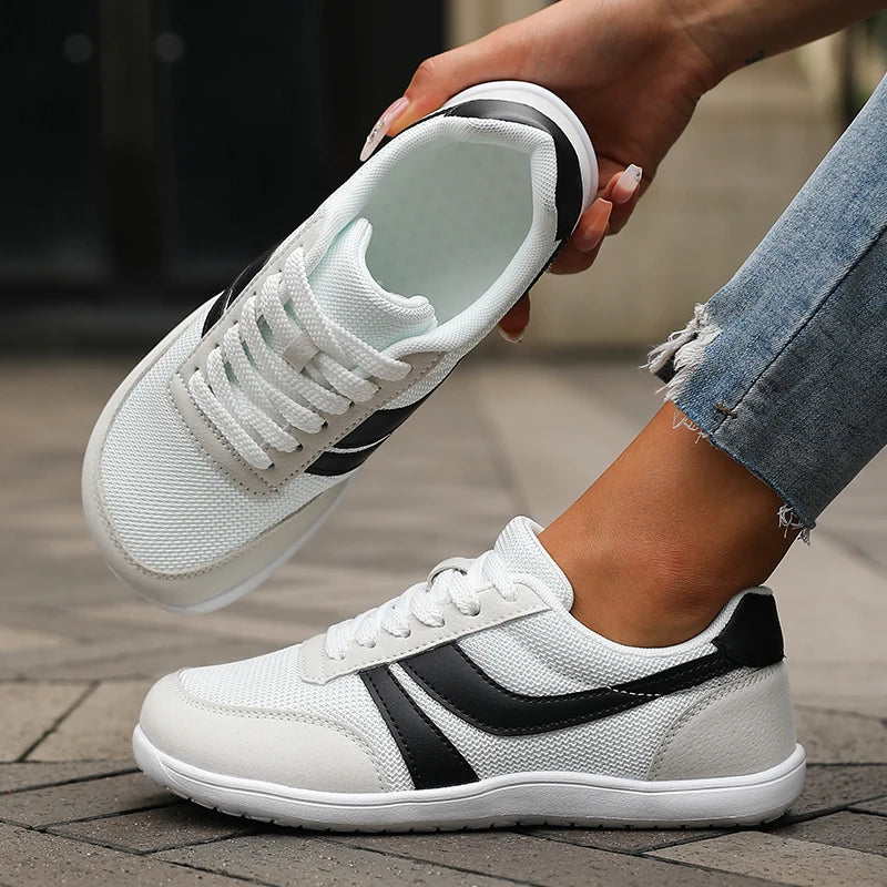 White sneakers with black accents held by a person wearing jeans on a wooden floor.
