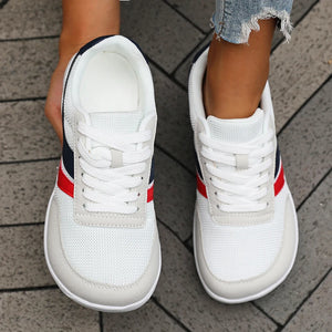 White sneakers with red and blue stripes on a pavement background