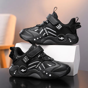 A pair of black children's sneakers with white graphic details and velcro straps, displayed on a white box and a dark surface.