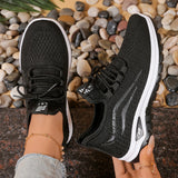 Black athletic shoes with white soles held by a person against a stone background