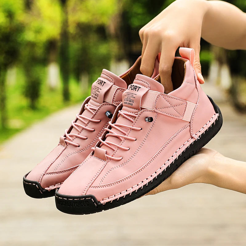 Pink sneakers with black soles held by a hand against a blurred green outdoor background