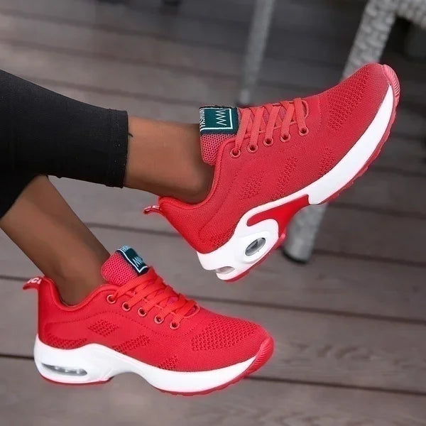 Red sneakers with white soles worn by a person on a wooden floor.