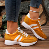 Yellow sneakers with white stripes worn by a person on a wooden surface.