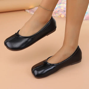 Black flat shoes worn by a person on a beige background