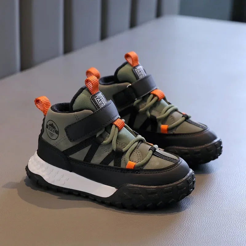 A pair of kids' outdoor high-top sneakers in olive green, black, and orange, displayed on a gray textured surface.
