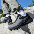Person wearing black hiking shoes on a rocky surface with a clear blue sky.