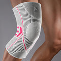 White knee brace with pink accents on a person's knee against a gray background