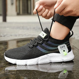 Person tying a black athletic shoe with white sole on a wet pavement.