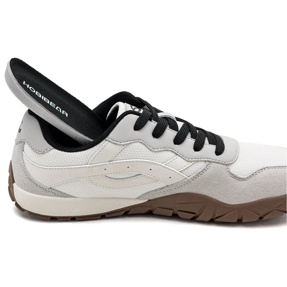 A white and light gray athletic shoe with black laces, a black interior lining, and a brown outsole, shown in a side profile on a white background.