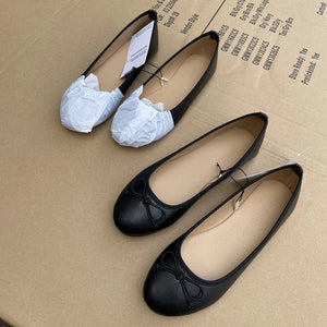 Black flat shoes with white bows on a cardboard surface