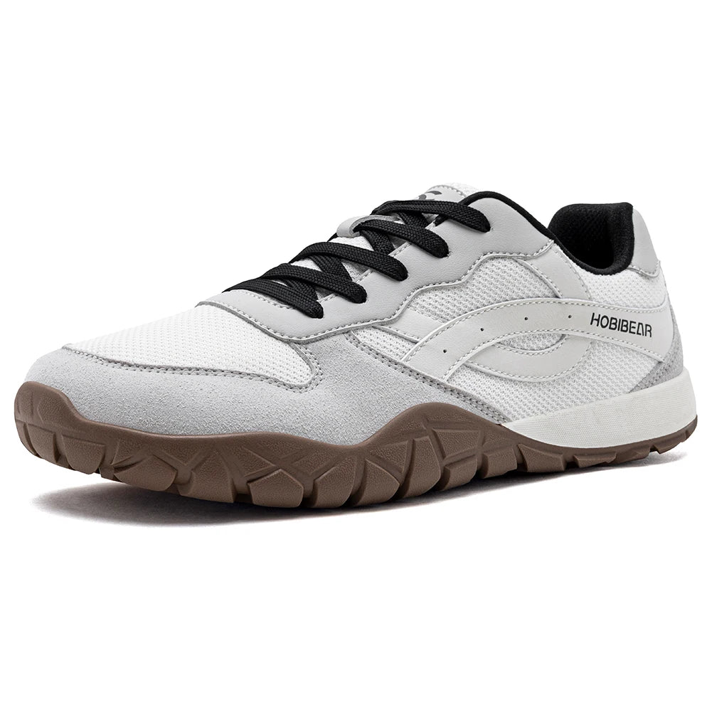 A white and light gray athletic sneaker with black laces, a black interior lining, and a brown textured sole, shown from a three-quarters angle on a white background.