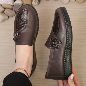 Brown leather shoe with decorative elements on a wooden floor.