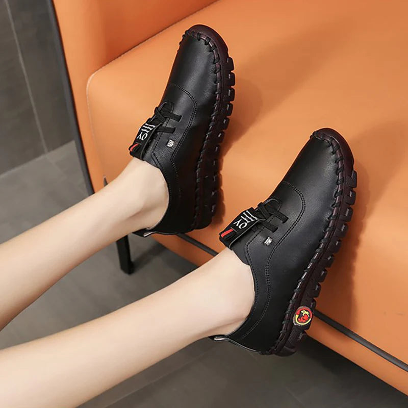 Black leather shoes worn by a person sitting on an orange chair.