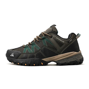 A single hiking shoe shown in a side profile on a clean white background. The shoe features a dark gray and black mesh and suede upper with olive green accents, tan midsole, and a rugged black outsole with small orange details.