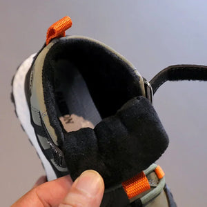 A close-up of a winter boot with a thick black fleece lining and an orange pull tab, held by a hand against a neutral gray background.