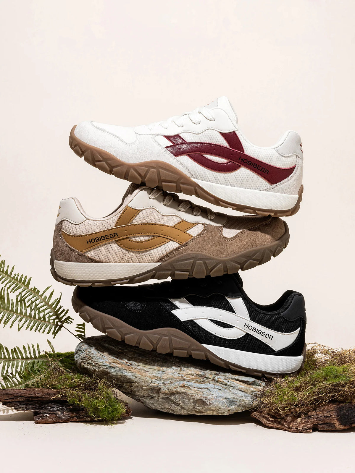 Three pairs of sneakers stacked on a natural background with greenery.