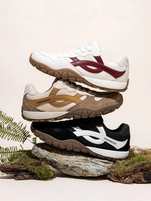 Three pairs of sneakers stacked on a natural background with greenery.