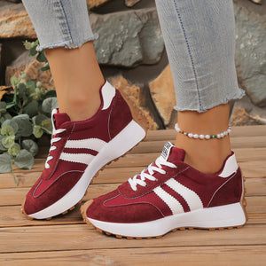 Red sneakers with white stripes worn on a wooden surface with a stone wall background