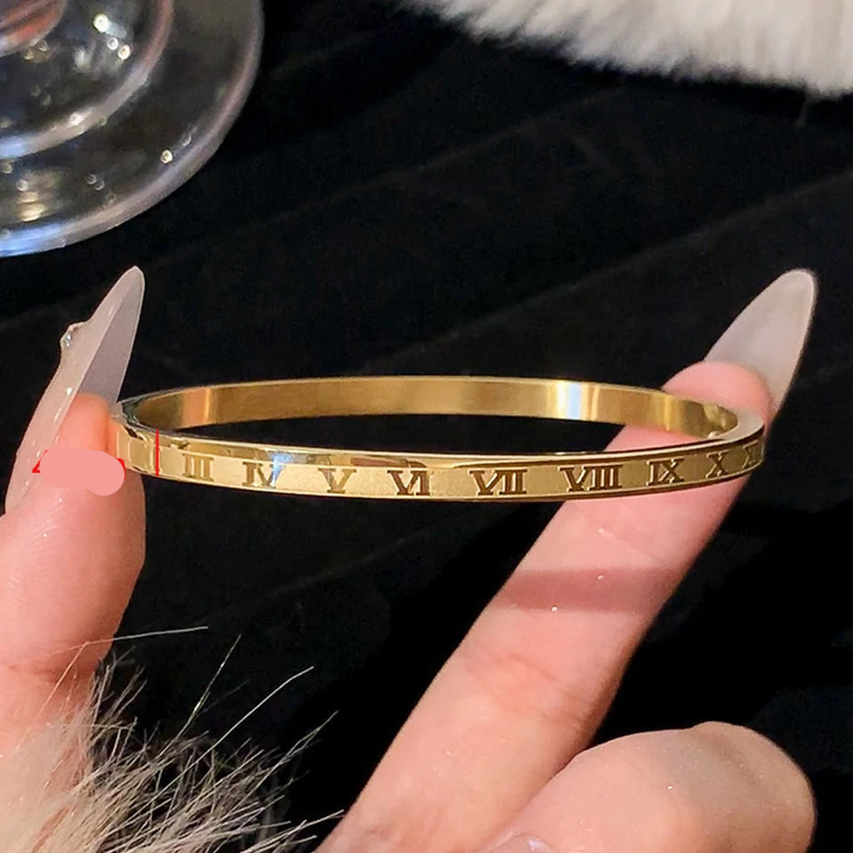 Gold bangle with Roman numeral design on a hand against a dark background