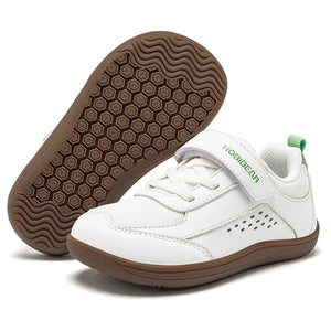White toddler's low-top casual shoe with a hook-and-loop strap and brown sole, shown alongside its brown textured outsole on a white background.