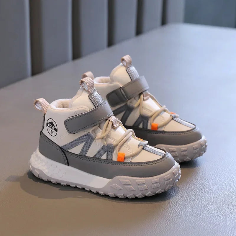 A pair of children's mid-top winter sneakers in white and gray with small orange accents, displayed on a gray textured surface.