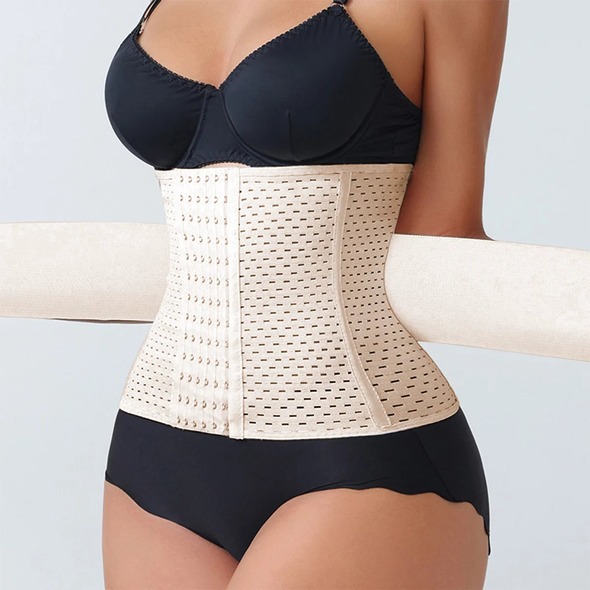 Person wearing a beige waist trainer with a black bra and underwear set on a light gray background