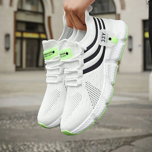 White sneakers with black stripes and green accents held by a hand, blurred background